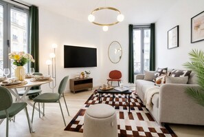 Uma sala de estar moderna com sofá, mesa de jantar posta para dois, TV na parede e tapete estampado.