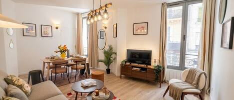 A modern living room with a sofa, dining table, chairs, a TV, and a balcony with curtains.