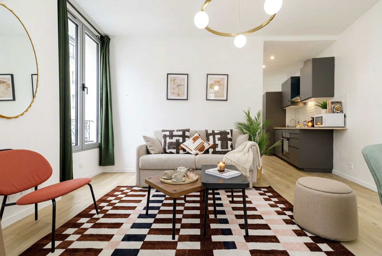 A modern living room with a sofa, a coffee table, and a dining table. There is a kitchen area with cabinets and a microwave.