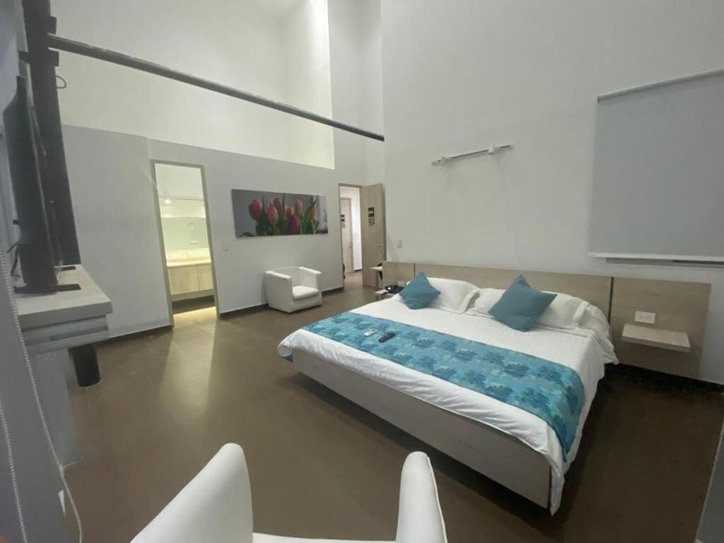 A modern hotel room with a large bed, a desk, a chair, and a painting on the wall.