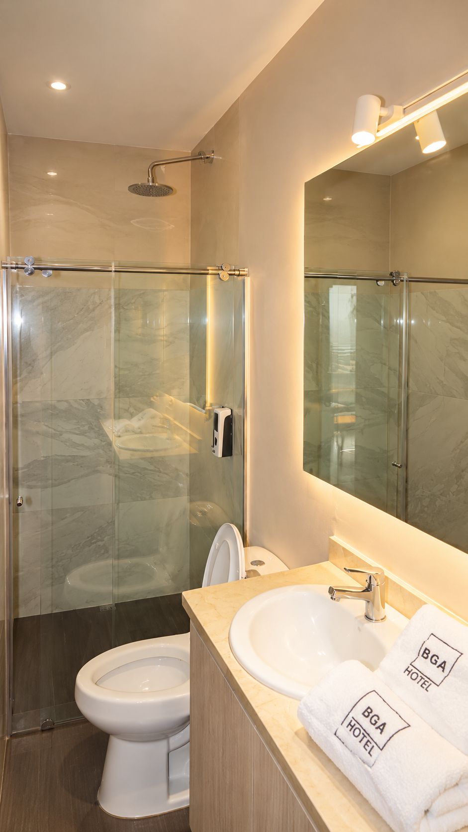 Un baño moderno con ducha envuelta en cristal, inodoro, lavamanos y un espejo grande.