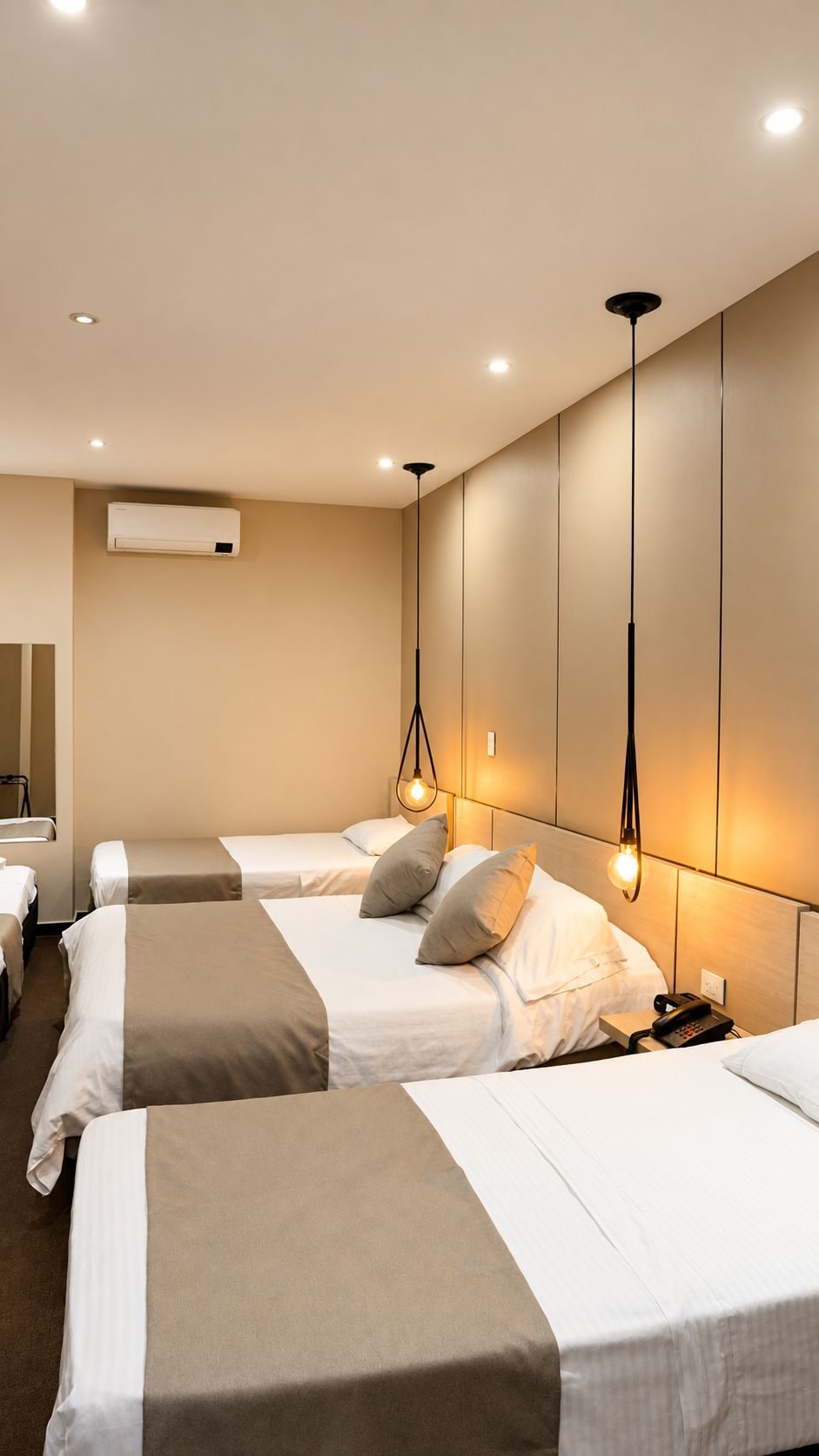 Une chambre d’hôtel avec trois lits, un appareil de climatisation et des lampes suspendues.