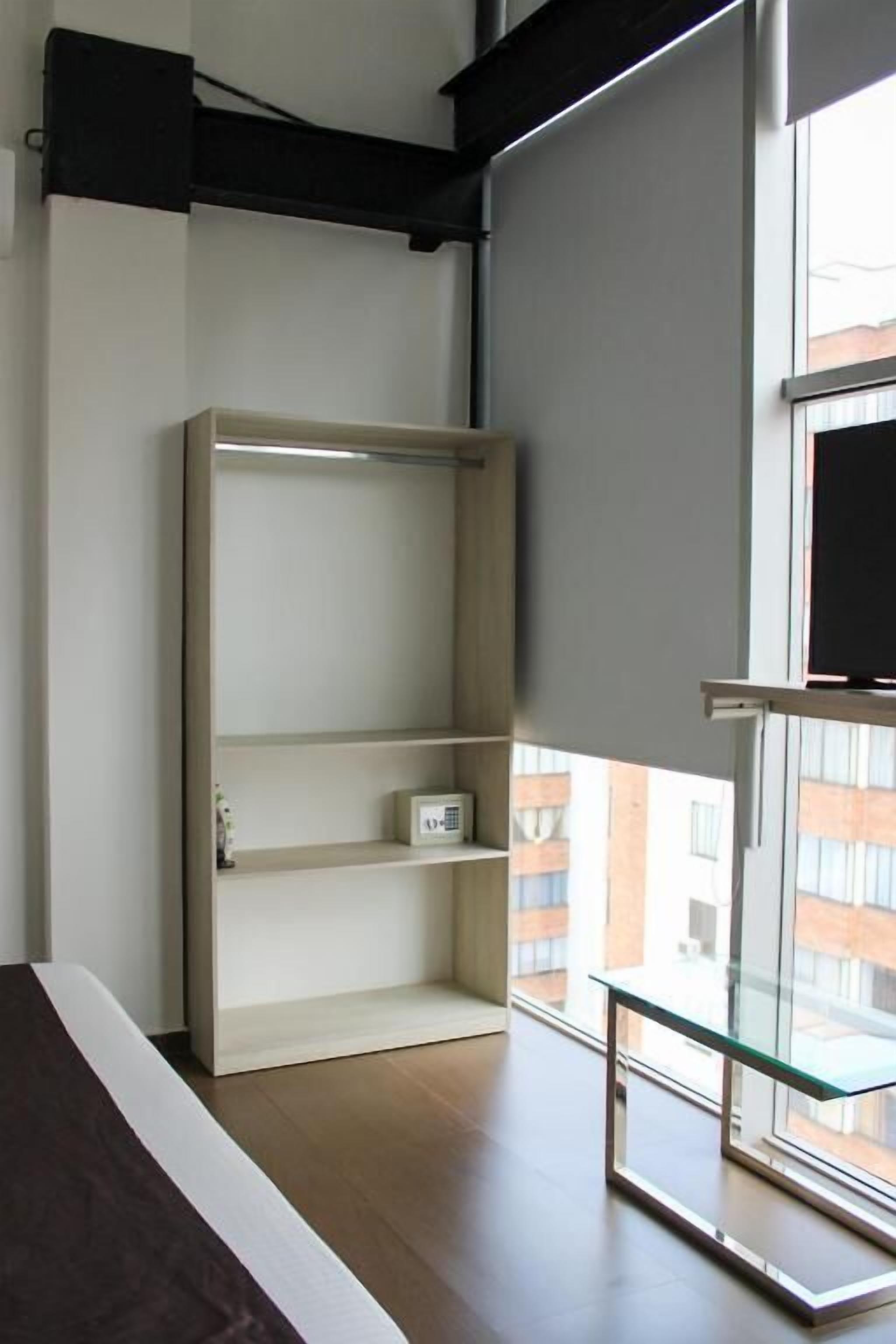 Una habitación con una estantería de madera, una mesa de vidrio y un ventanal con vistas a edificios.