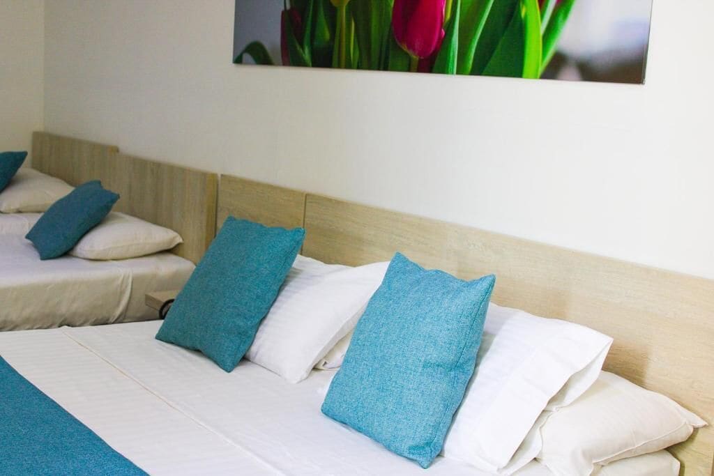 A hotel room with a bed, pillows, and a wall-mounted picture of flowers.