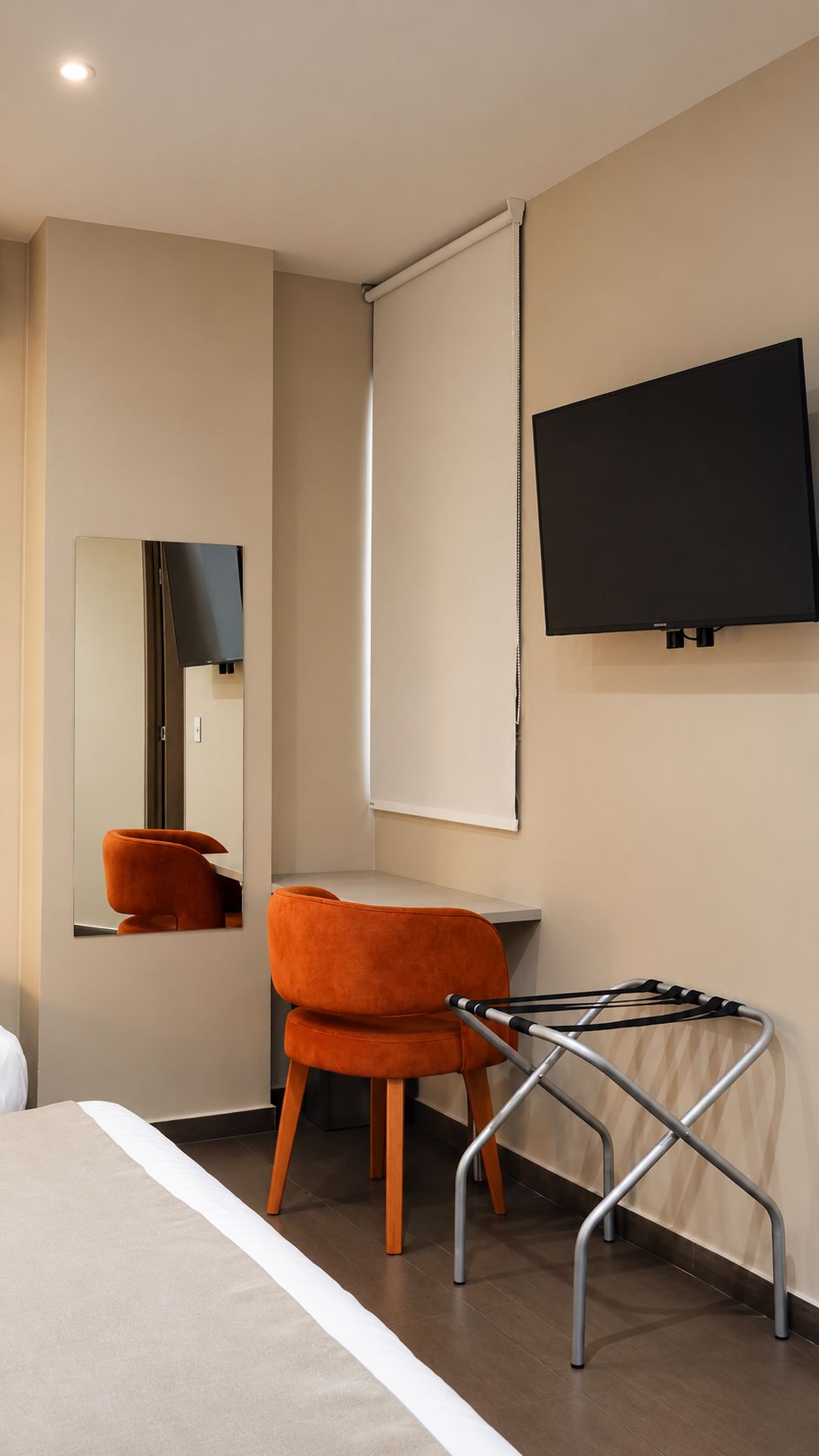 Una habitación de hotel con cama, una silla, un televisor y un espejo.