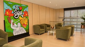 Un vestíbulo moderno con sillones verdes, una mesa de centro de vidrio y un mural grande en la pared.