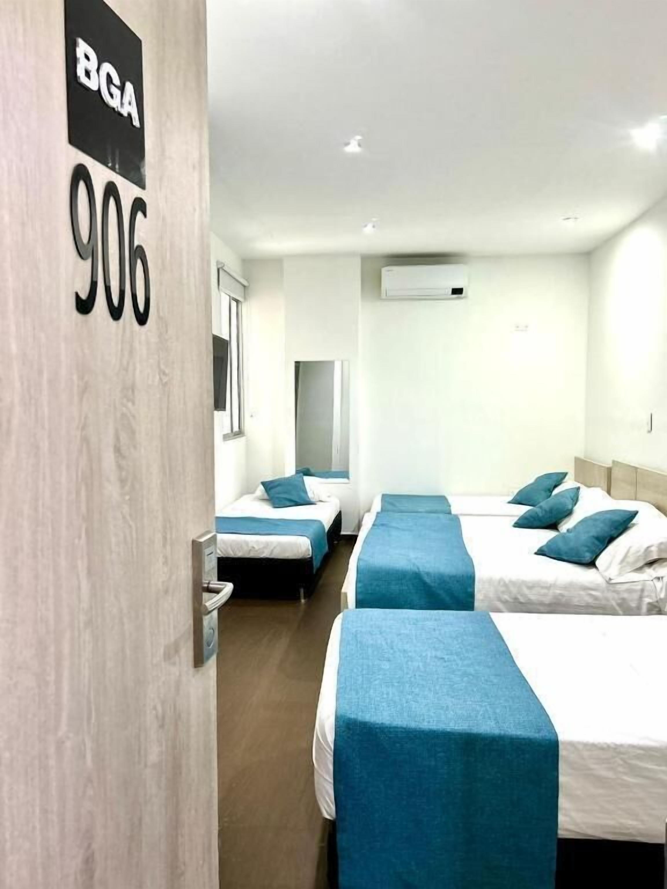 A hotel room with three beds, a wooden wall with a sign, and a window.