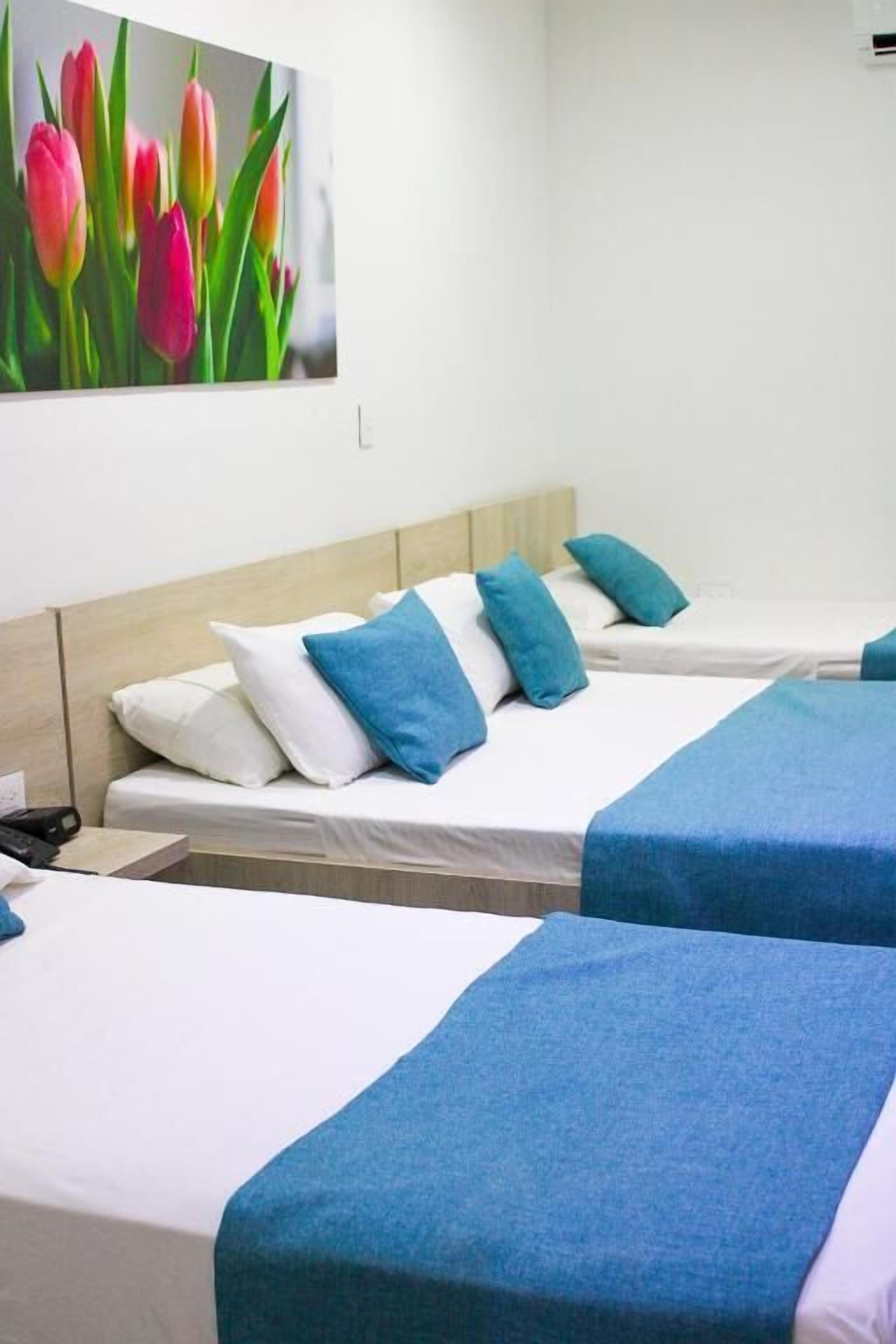 A hotel room with two single beds, each with a blue bedspread and white pillows.
