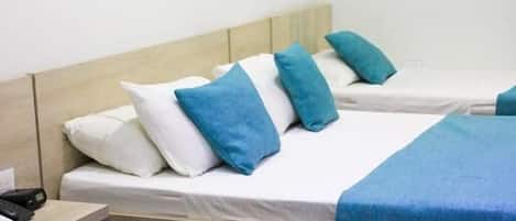 A hotel room with two single beds, each with a blue bedspread and white pillows.