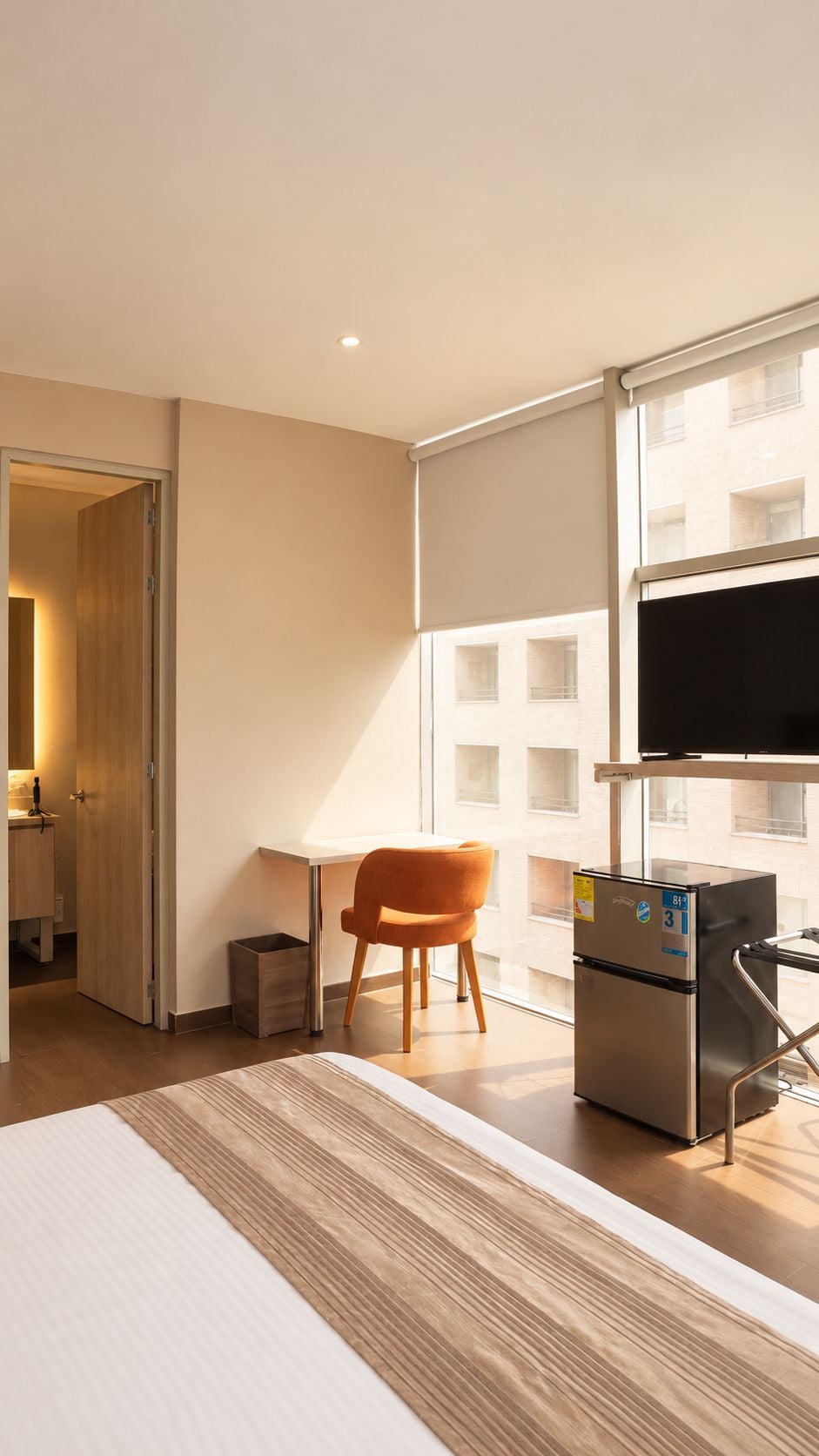 Una habitación de hotel con cama, escritorio, silla, televisor y refrigerador.