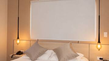 A hotel room with a bed, bedside tables, an air conditioning unit, and pendant lighting.