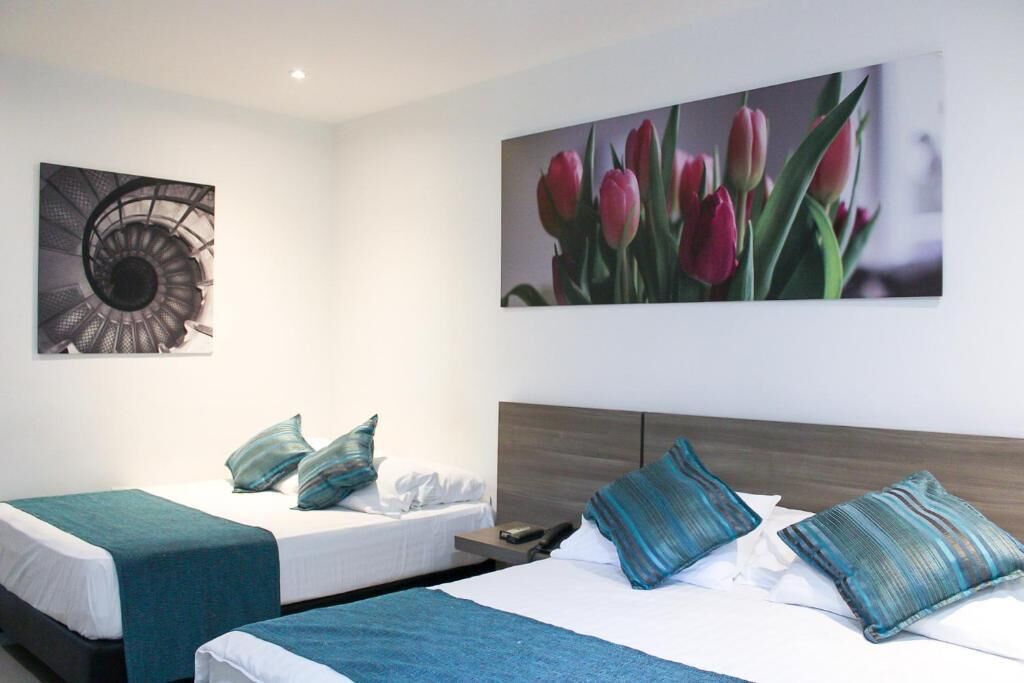 Habitación de hotel con dos camas, cabecero y una obra de arte colgada en la pared.