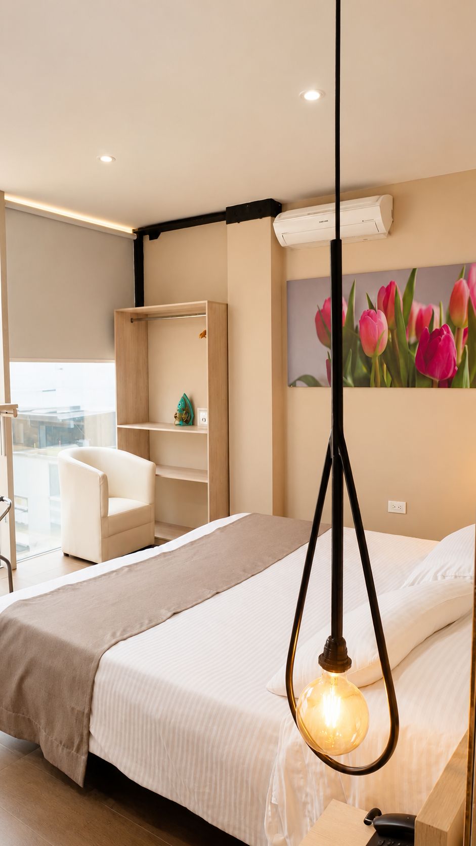 Una habitación de hotel con una cama, un escritorio, una silla, un cuadro de tulipanes y una lámpara colgante.