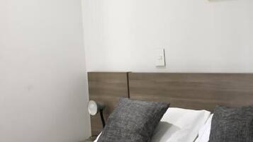 A bed with white and gray bedding, a wooden headboard, and a wall-mounted light fixture.