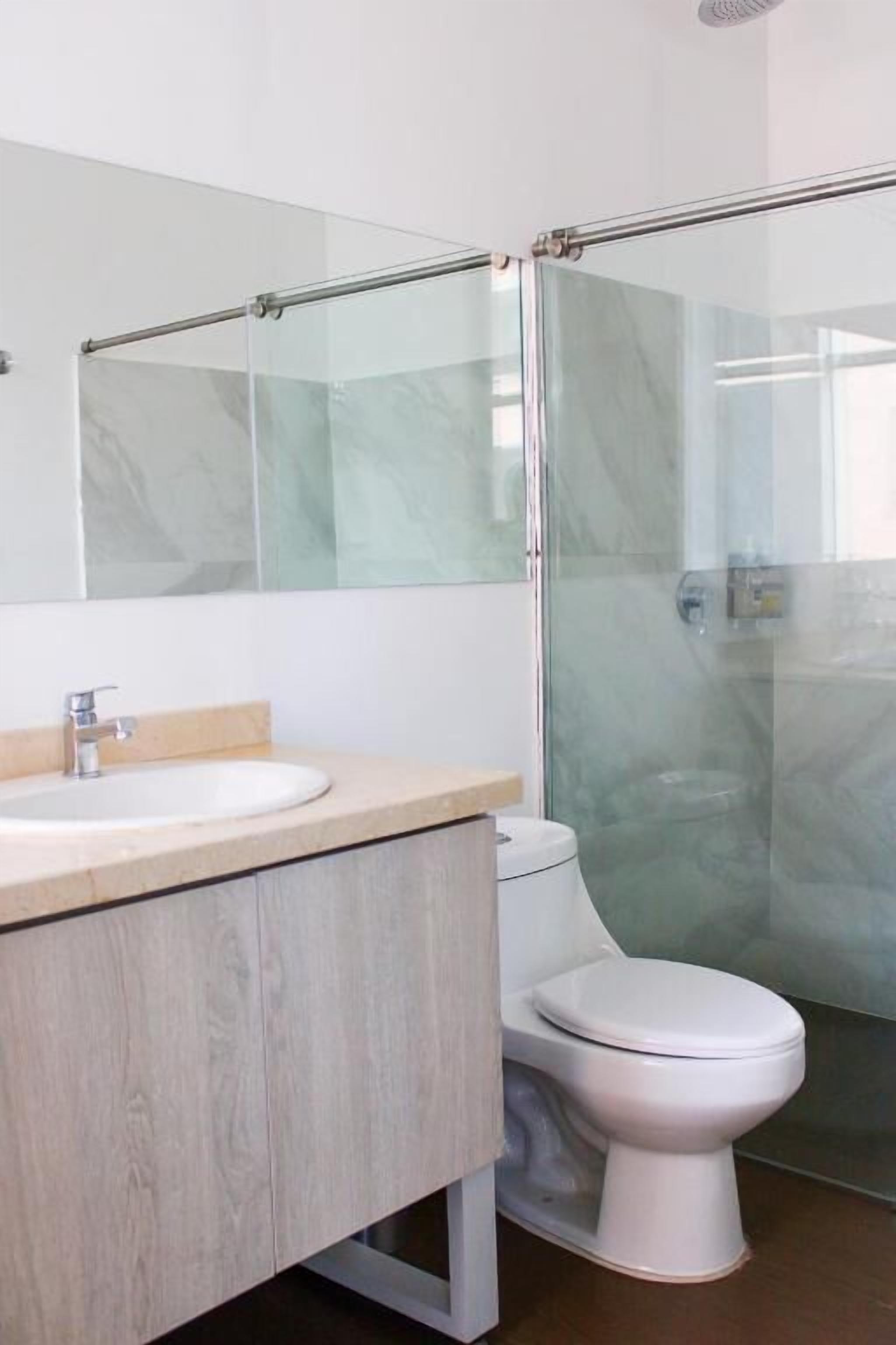 A modern bathroom with a glass shower enclosure, a white toilet, and a wooden vanity.
