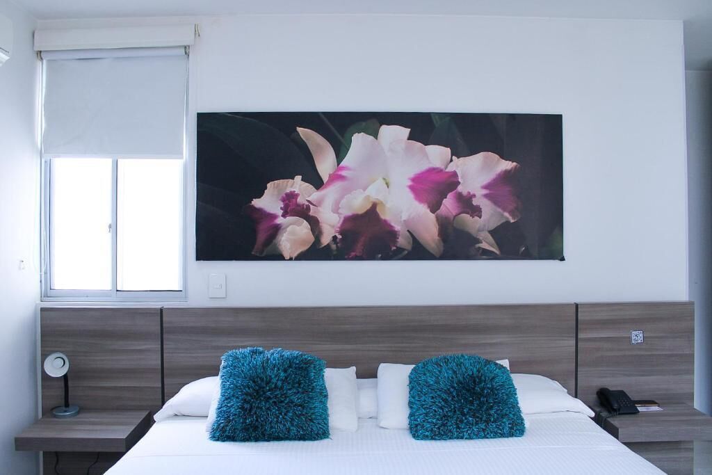 A bedroom with a bed, two pillows, a nightstand, a lamp, and a wall-mounted picture of flowers.