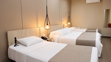 Habitación de hotel con tres camas, una mesita de noche con teléfono y aire acondicionado instalado en la pared.