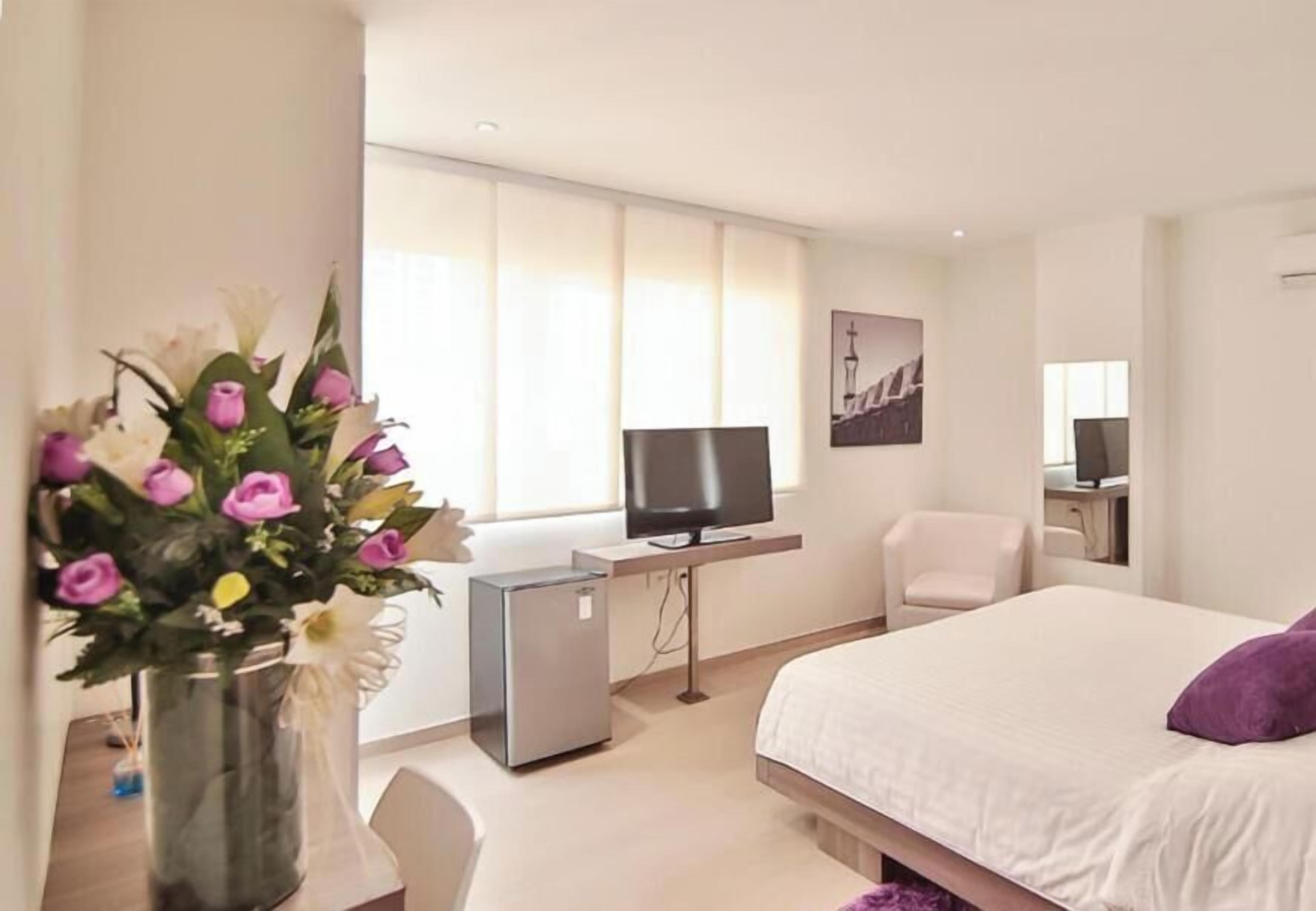 Habitación de hotel con cama, escritorio, televisor, una silla y un florero.