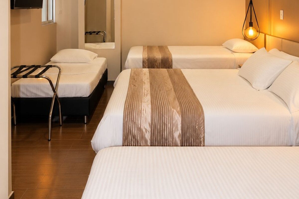 Habitación de hotel con dos camas, televisión, aire acondicionado y lámpara de noche.