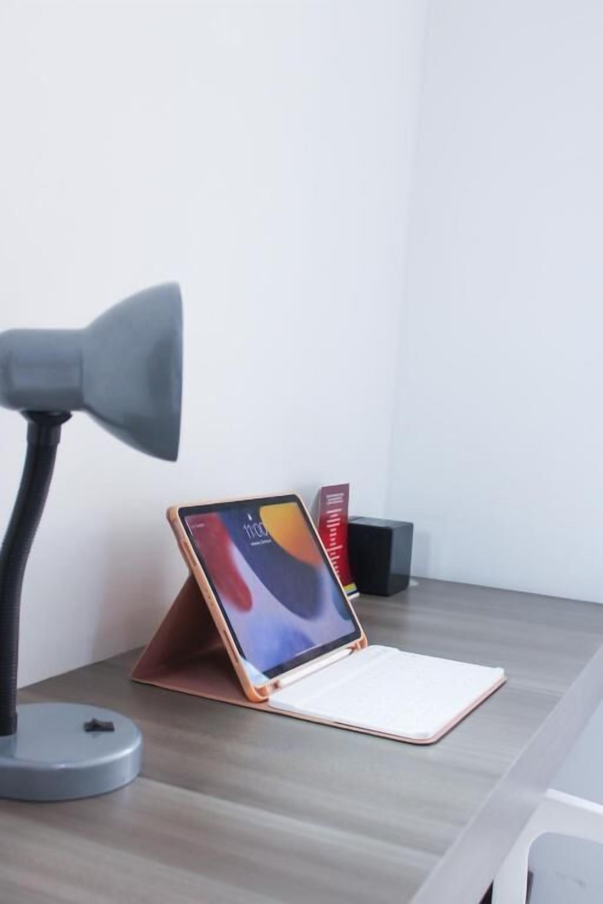 A desk with a tablet on a stand, a lamp, and a book.