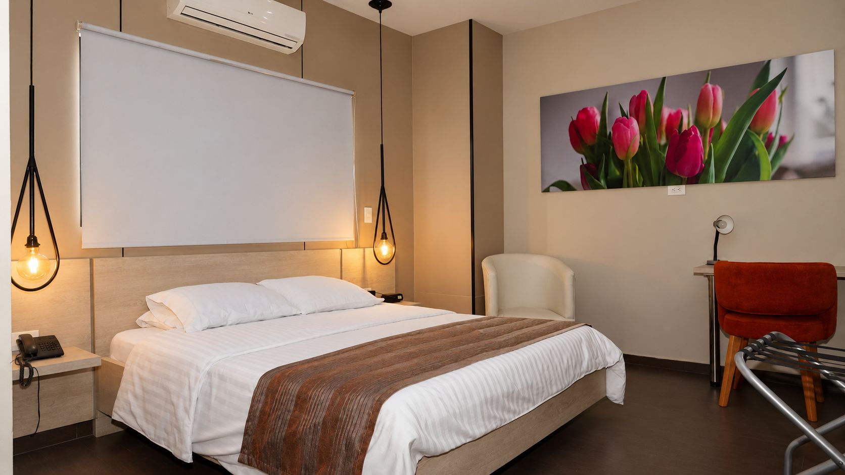 A hotel room with a bed, a whiteboard, a painting of tulips, a chair, and a desk with a red chair.