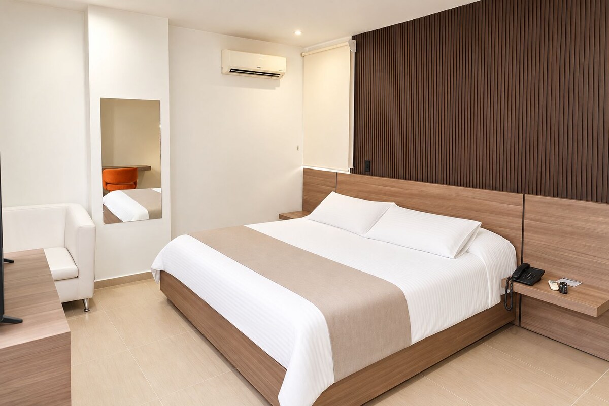 Una habitación de hotel moderna con una cama grande, una mesita de noche con teléfono, una silla y un aire acondicionado de pared.