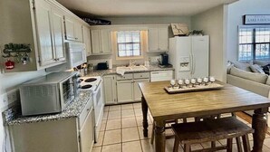 A compact kitchen with white cabinets, a microwave, a stove, and a dining table with chairs. - The Escape on Blade Bay (Hardin County)