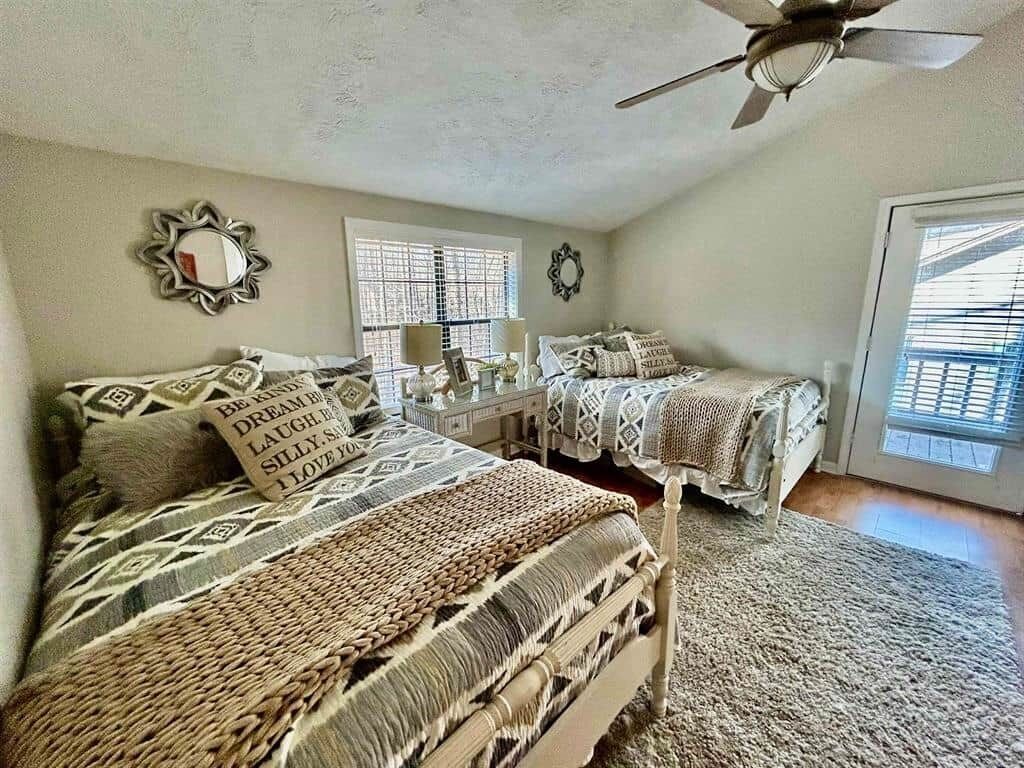 A bedroom with two beds, a ceiling fan, and a large window.