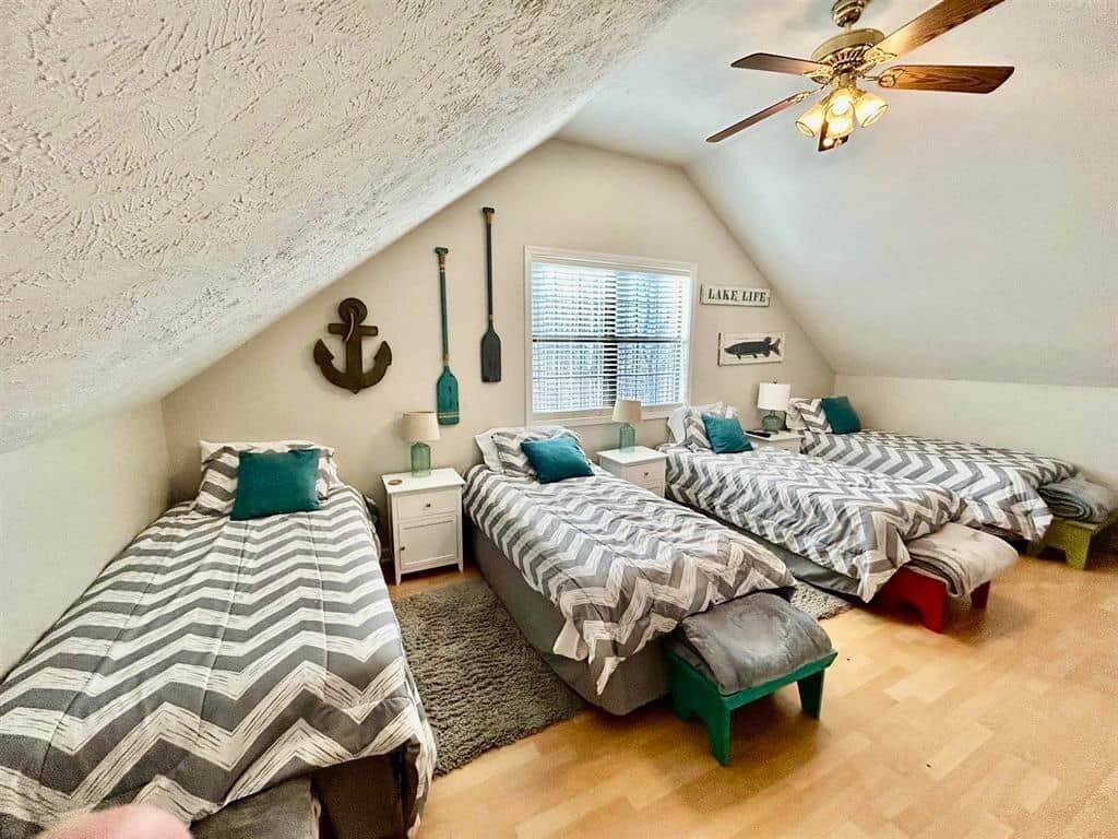 Un dormitorio con dos camas, un ventilador de techo, una ventana con persianas y un adorno fijado a la pared.