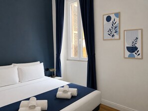 A hotel room with a bed, a window with curtains, and two wall art pieces.