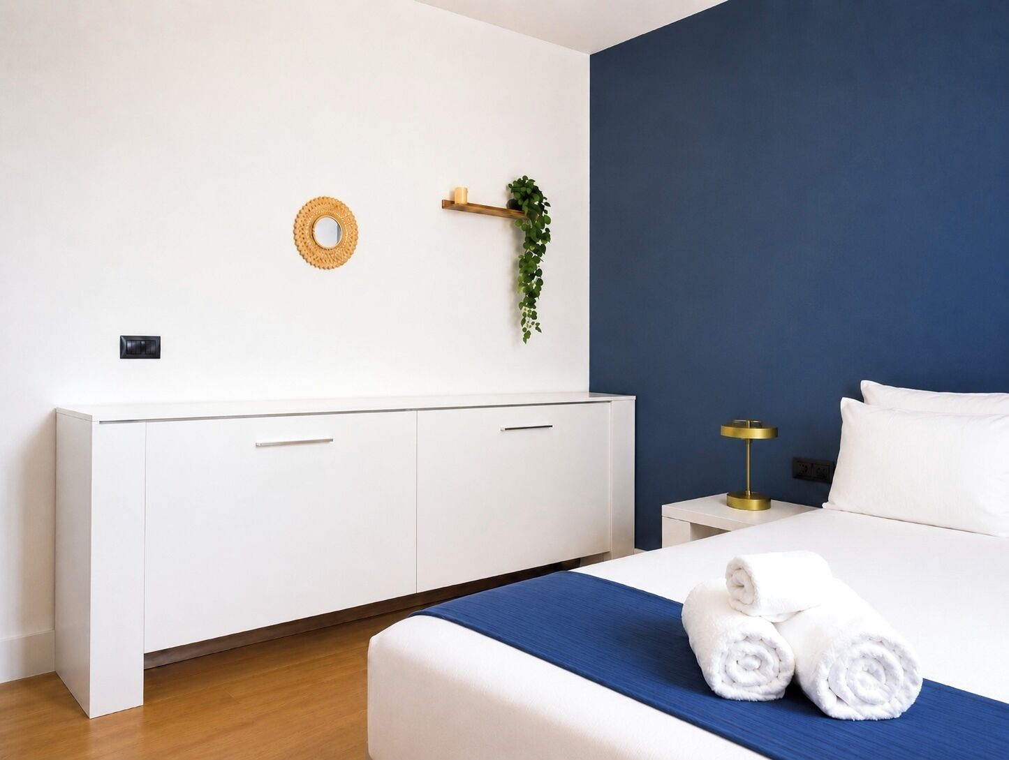 Ein Hotelzimmer mit einem Bett, einem Nachttisch, einem weißen Kleiderschrank, einem wandmontierten Spiegel und einer kleinen Pflanze.
