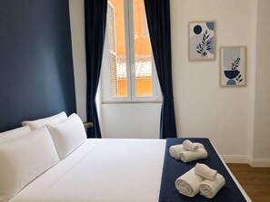 Hotellihuone, jossa on sänky, ikkuna, jossa on verhot, ja kaksi seinätaideteosta.