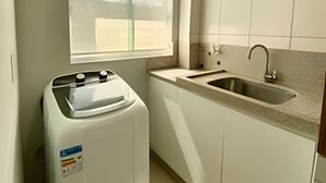Cocina compacta con lavadora integrada, un lavamanos y una ventana.