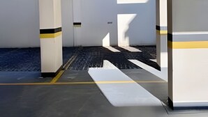 Un garaje para estacionar con paredes blancas, franjas amarillas y negras, y piso de concreto.