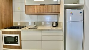 Una cocina compacta con microondas integrado, estufa a gas, lavamanos y refrigerador.