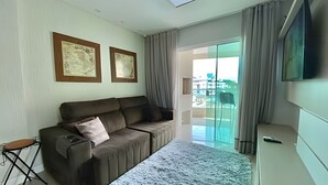 Sala de estar moderna com sofá, uma mesinha, televisão de tela plana e vista para o exterior.