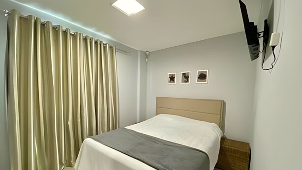 Quarto com cama, cortinas, mesa de cabeceira e tomada na parede.
