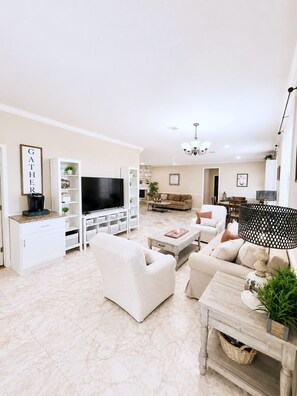 A spacious living room with a flat-screen TV, white sofas, a coffee table, and a fireplace. - Millican Farmhouse 5 Acre Retreat - 10 min to Aggieland! (Navasota)