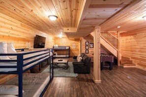 A cozy cabin interior with bunk beds, a sofa, a coffee table, a foosball table, and a staircase. - 5 Minutes to Ash Cave! Sleeps 10 w/3 Private Bedrooms + Hot Tub + WiFi + Games (South Bloomingville)