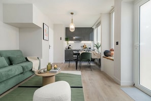 A modern living room with a green sofa, a coffee table, and a white armchair. There is a kitchen in the background with a dining area. - PoeticStay - Montmartre - Dunkerque (Paris)