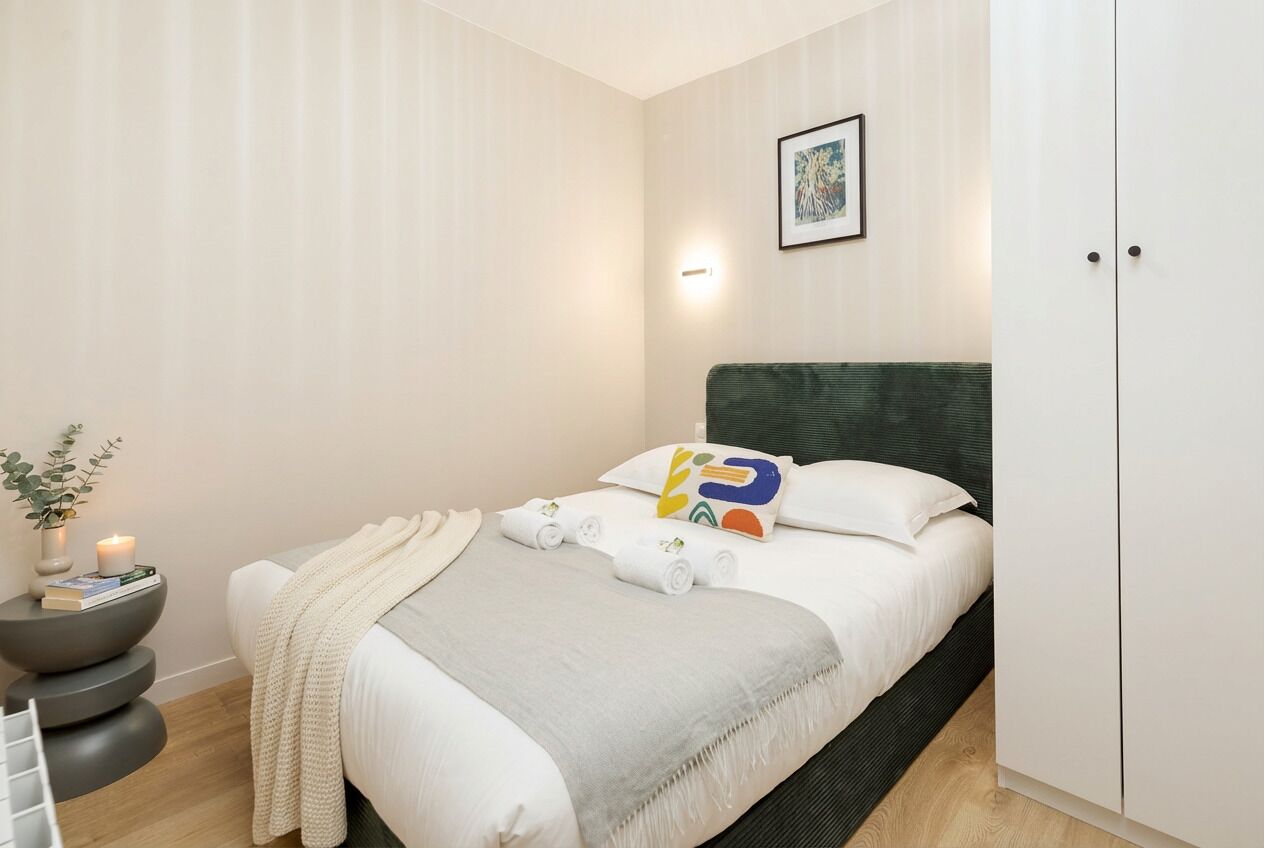 A hotel room with a bed, bedside table, and a wardrobe.