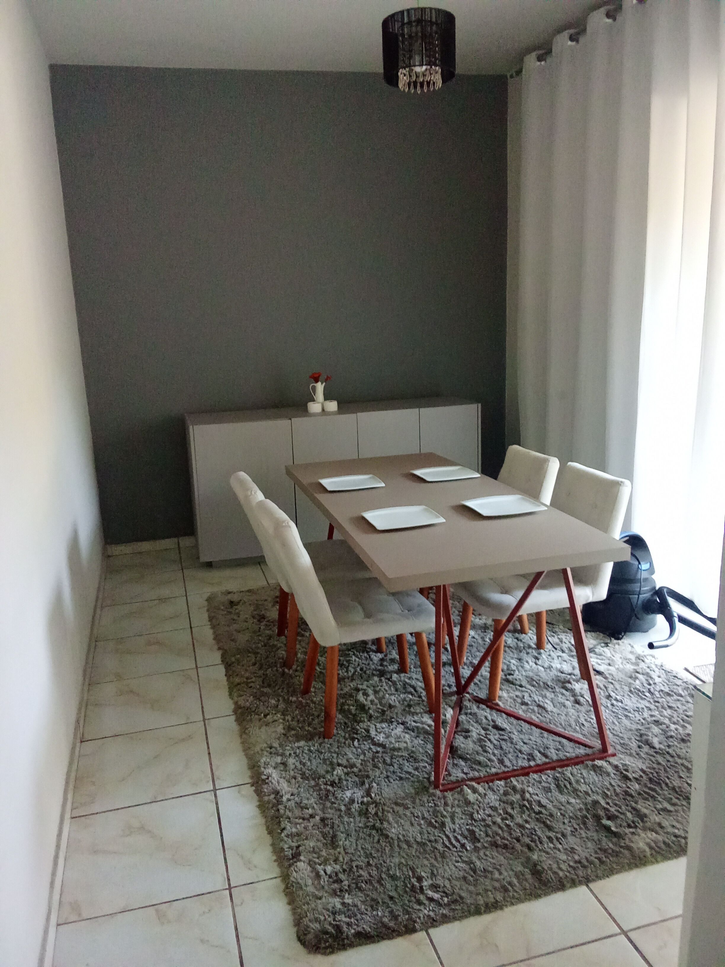 A dining area with a table set for four, a grey rug, and a grey wall.