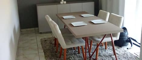 Un comedor con una mesa dispuesta para cuatro personas, un tapete gris y una pared gris.