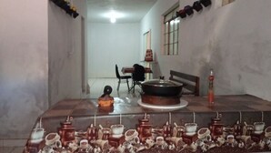 A dining area with a table set for two, a chair, a small table with a pot, and a bottle on the floor.