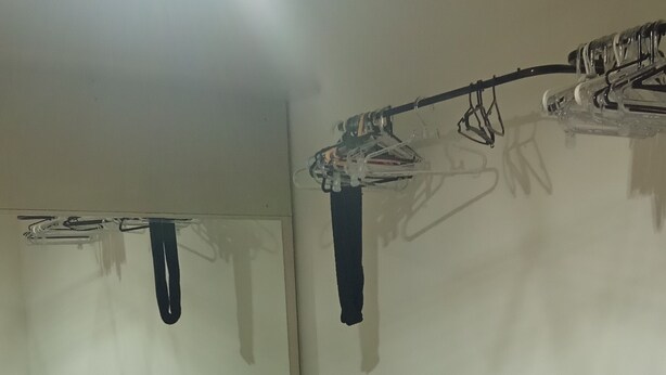 A room with two beds, a bench, a mirror, and a clothing rack.
