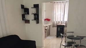 A living room with a black sofa, a wooden dining table, and a kitchen area in the background.