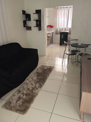 A living room with a black sofa, a wooden dining table, and a kitchen area in the background.