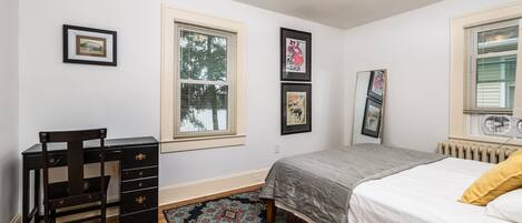 A bedroom with a bed, a desk, and a chair. There are three framed pictures on the wall.