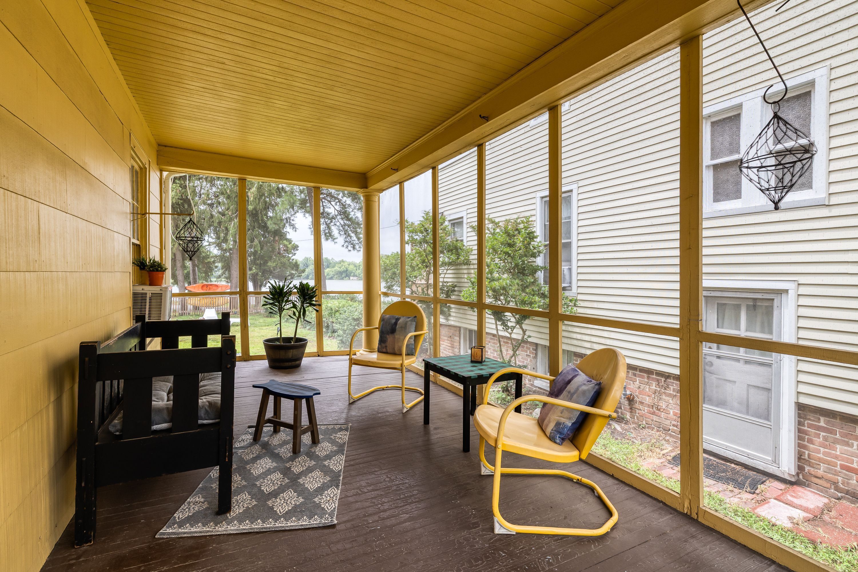 A covered porch with wooden flooring, a table, chairs, and a hanging light fixture.