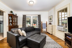 Un salon avec un canapé en cuir noir, un meuble en bois, un radiateur et un téléviseur.